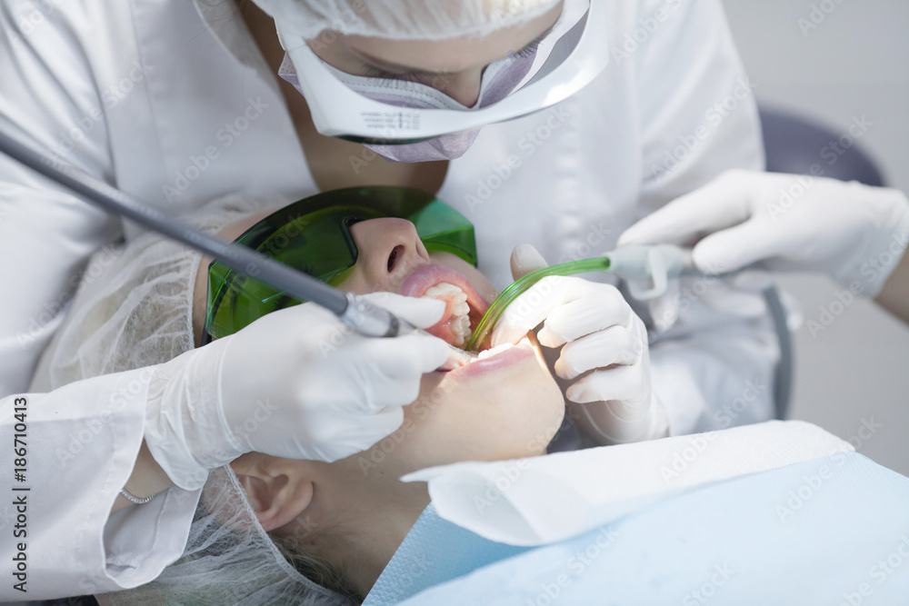 Naklejka premium Young female patient visiting dentist office.Beautiful woman with healthy straight white teeth sitting at dental chair with open mouth during a dental procedure.Dental clinic. Dental caries