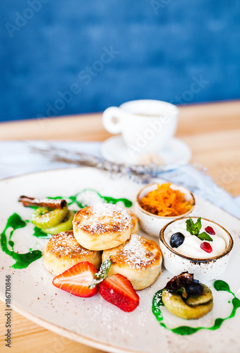 beautiful breakfast: curd puncakes with cranberries, figs, strawberries and sour cream with a cup of coffee
