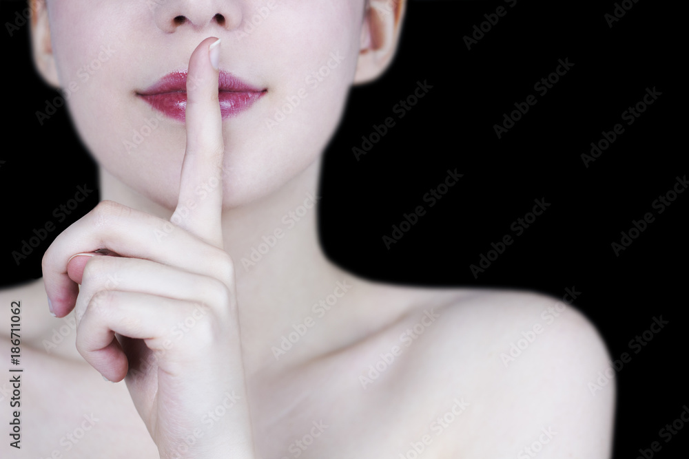 Naklejka premium Close up of young woman's face smiling with red lips showing silence gesture on black background - secret concept