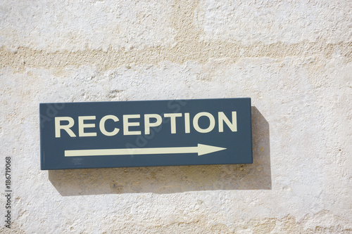 sign attached to a white wall indicating where the reception area is.