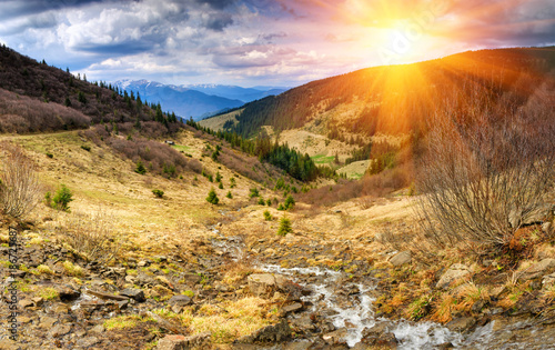 Panorama of idyllic landscape in the spring mountains at sunshine. View of the mountain stream flowing among the hills.