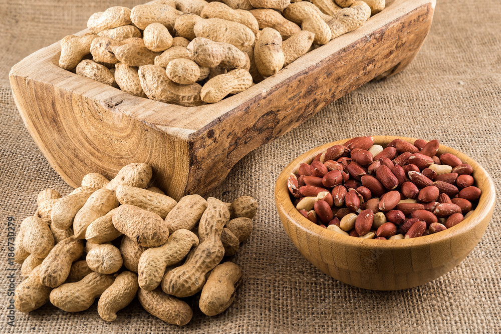 Peanuts in nutshell on a piece of wood and peeled peanuts in a bowl on sackcloth Peanuts in nutshell on a piece of wood and peeled peanuts in a bowl on sackcloth