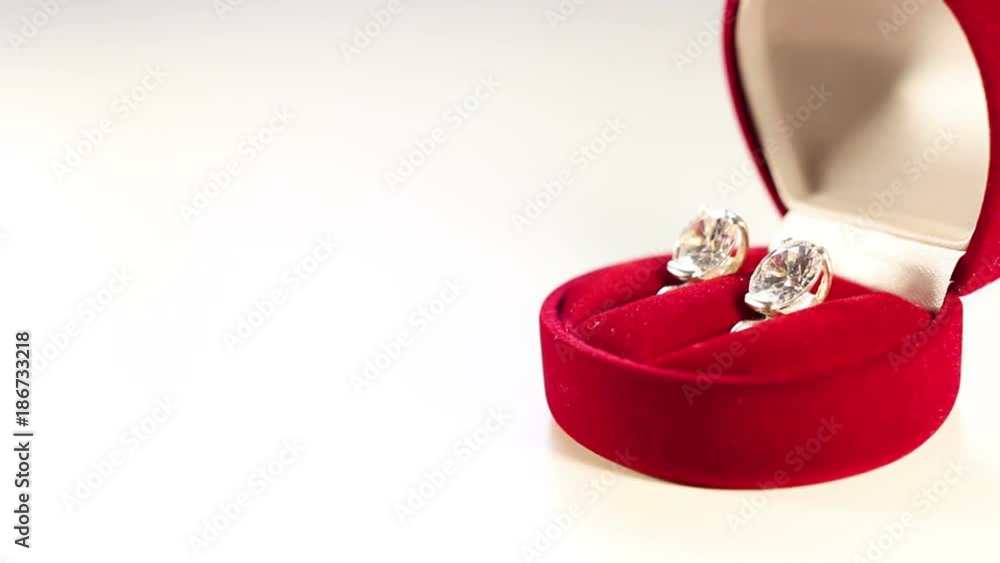 A man puts a gift red box with earrings on a white surface. A man puts a gift red box with earrings on a white surface.