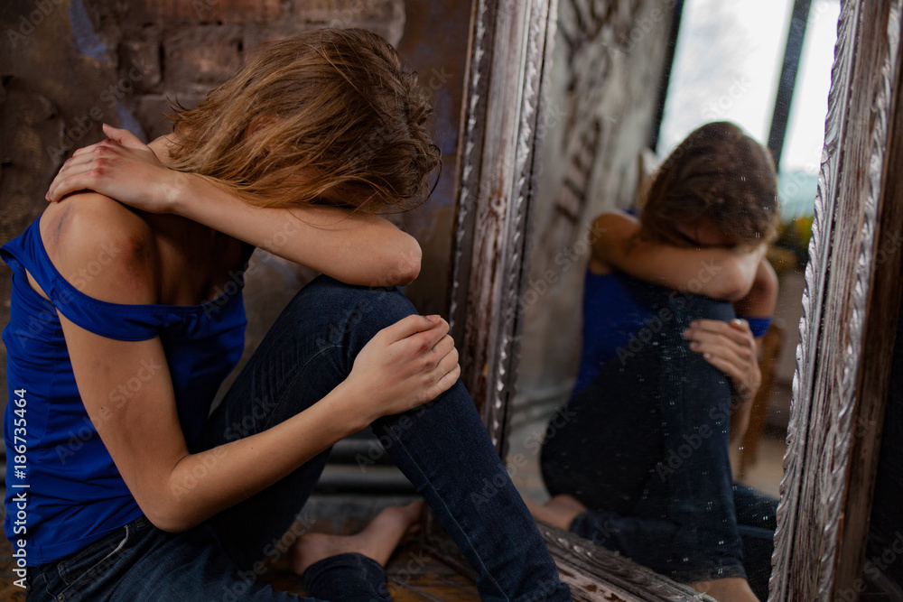 Woman victim of domestic violence and abuse cries and sits on floor near mirror with bruises and wounds on her body. Woman victim of domestic violence and abuse cries and sits on floor near mirror with bruises and wounds on her body.
