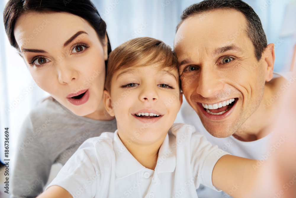 Upbeat mood. Adorable little boy taking a close-up selfie with his parents and all of them posing for the camera, smiling and making funny faces Upbeat mood. Adorable little boy taking a close-up selfie with his parents and all of them posing for the camera, smiling and making funny faces