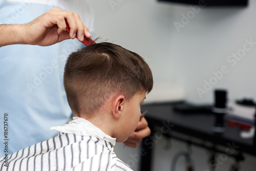 Barber shop. Hairdresser makes hairstyle to a boy.