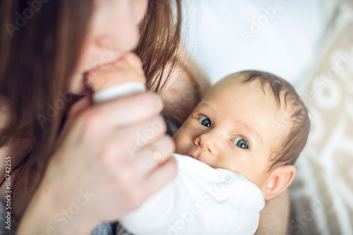 Happy caring mother holding a smiling baby boy in the bedroom. Concept of the tenderness of motherhood and family values