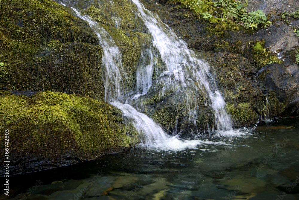 fragment of a small waterfall flowing over the mossy stones into a transparent lake..