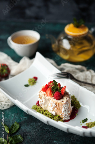 light dessert Anna Pavlova with raspberries and pistachios with a teapot and a cup of tea on a dark green concrete background