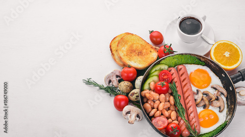 English breakfast tomatoes, sausages, beans, mushrooms, eggs,toast and herbs top view. On a white wooden background.