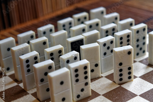 Domino pieces in a row and one different statnd, on the bamboo brown wooden table background photo