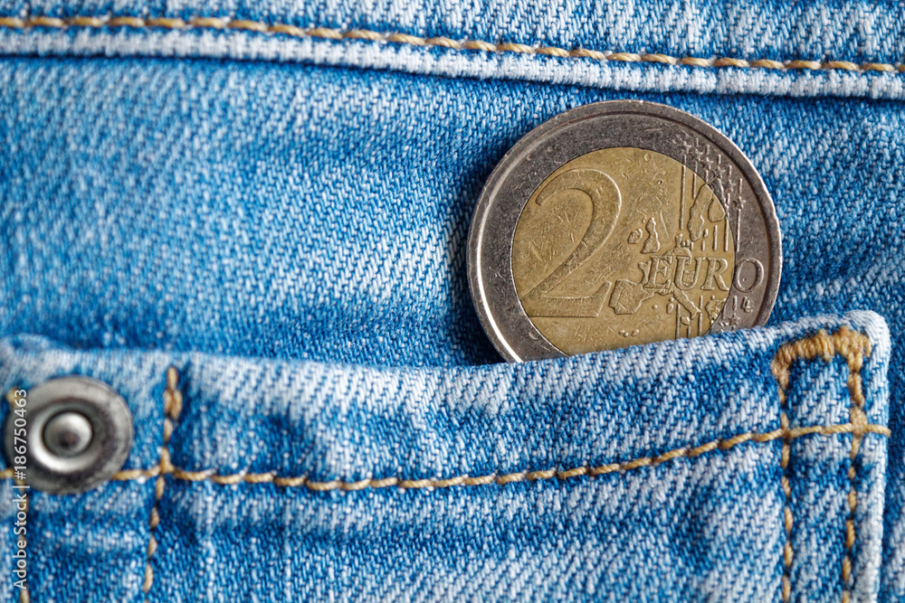 Euro coin with a denomination of 2 euro in the pocket of dark blue denim jeans Euro coin with a denomination of 2 euro in the pocket of dark blue denim jeans