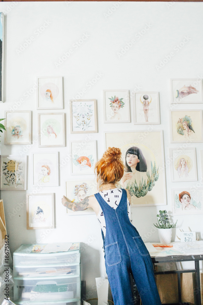 Rear view of female artist hanging paintings on wall in studio Rear view of female artist hanging paintings on wall in studio