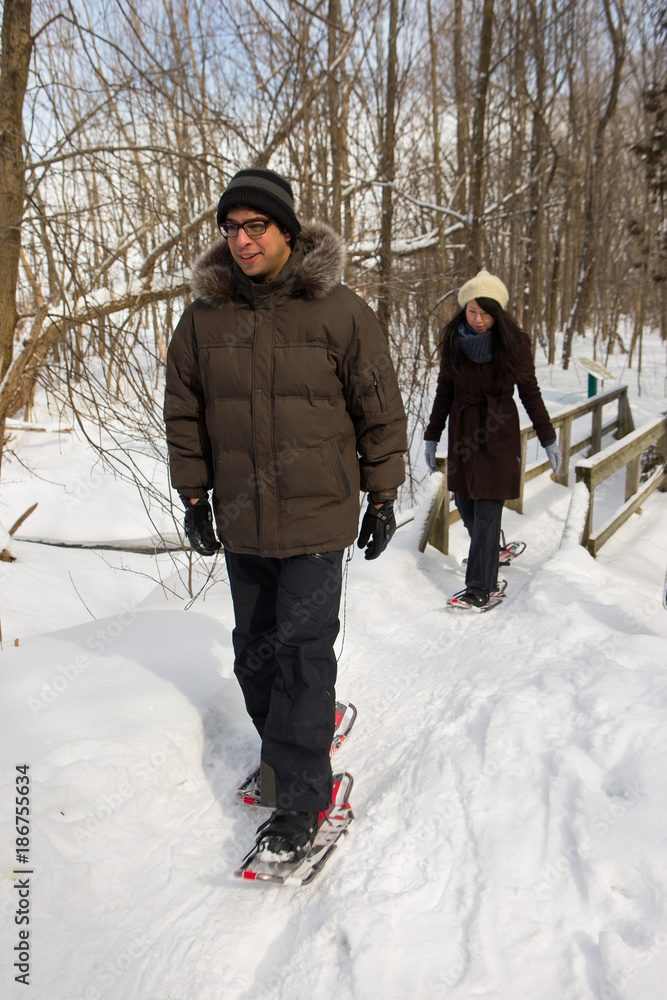Naklejka premium Ethnic couple snowshoeing in the forest near a waterfall
