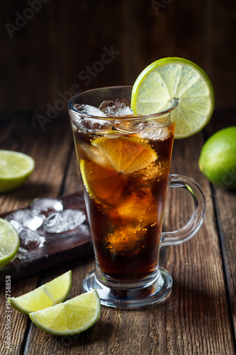 Rum and cola Cuba Libre drink with brown rum, cola, ice and lime on rustic wooden table