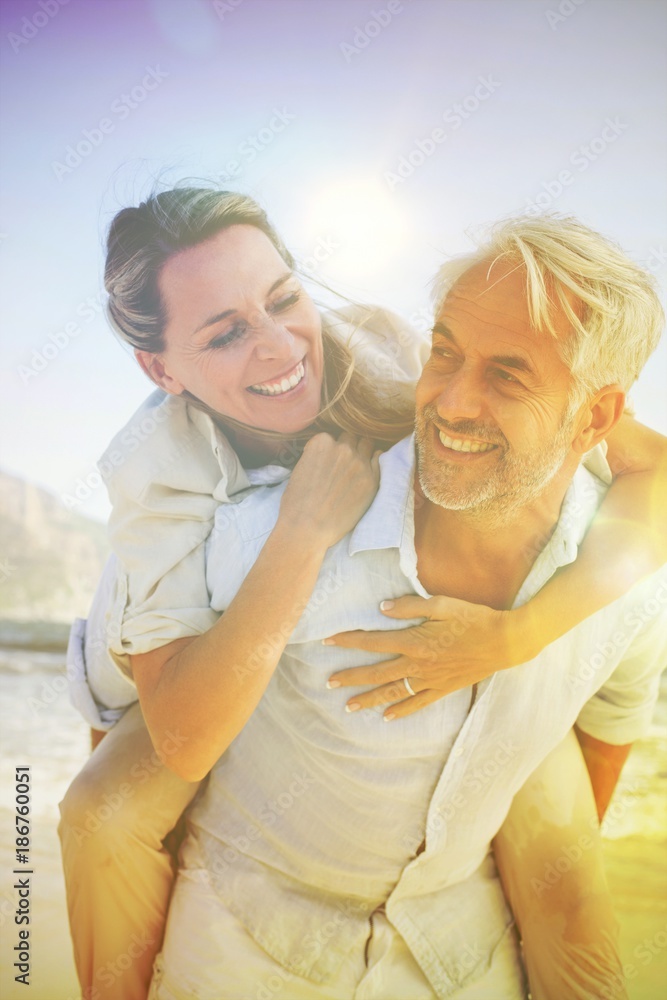 Obraz premium Man giving his smiling wife a piggy back at the beach