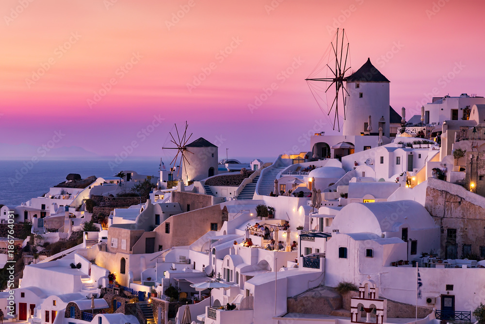 Fototapeta Die Windmühlen und weißgewaschenen Häuser von Oia, Santorini, Griechenland, bei Sonnenuntergang