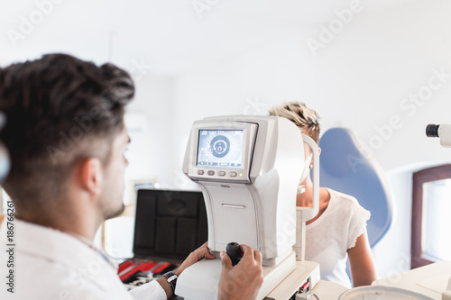 Photos Male optometrist examining with his patient at eye clinic.