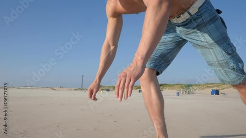 Pull-ups - man fitness model training on the beach outdoors.