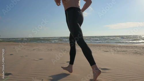 Handsome fit athletic male jogging on beach in sunny weather