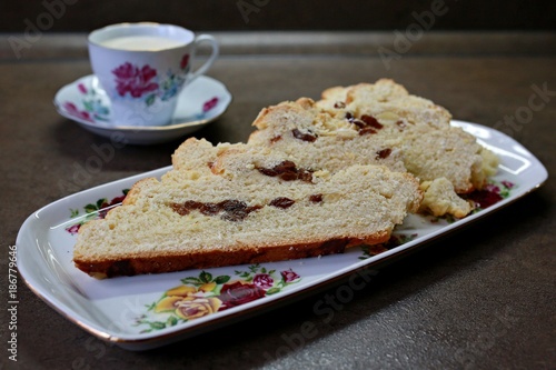 Traditional homemade Czech braided bread freshly baked and sliced on a ceramic tray with raisins and almonds with a flower cup of coffe in the background, placed on brown table