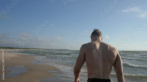 Handsome young man walking at the beach in swimming trunks