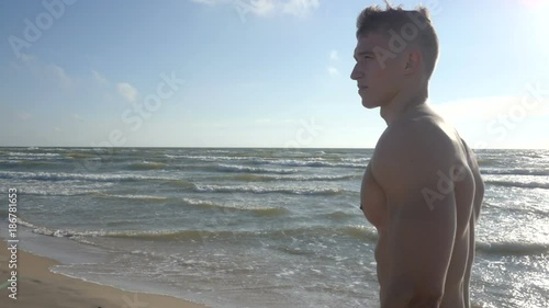 Handsome wet muscular man walking on beach