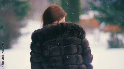 Close-up of Brunette fashionable sexy pretty rich woman or glamour model girl with beautiful long hair in waist coat of brown fur in winter with flying hair in motion posing for camera. slow motion photo