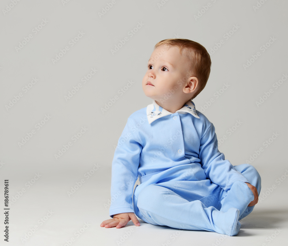 Infant child baby boy kid toddler sitting in light blue body cloth looking at the corner