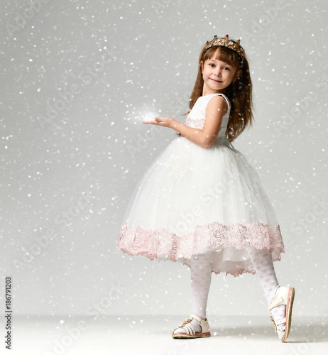 Fotografie Young little girl model in the white communion  winter dress stands in gold crow