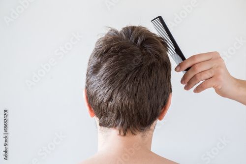 Hairdresser's hand with comb brushing man's dry brown hair on the gray background. Cares about a healthy and clean hair. Beauty salon concept.