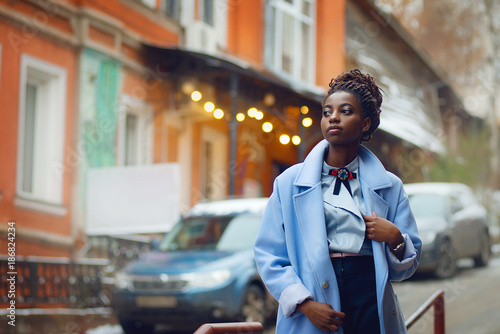Stylish African girl in the blue coat in the style fashion on the streets with bokeh and cars in the background
