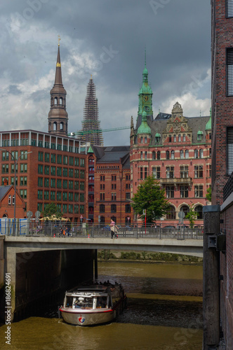 HAMBURG, GERMANY - JULY 18, 2015: ferry on the canal of Historic Speicherstadt houses and bridges at evening with amaising skyview over warehouses, famous place Elbe river.