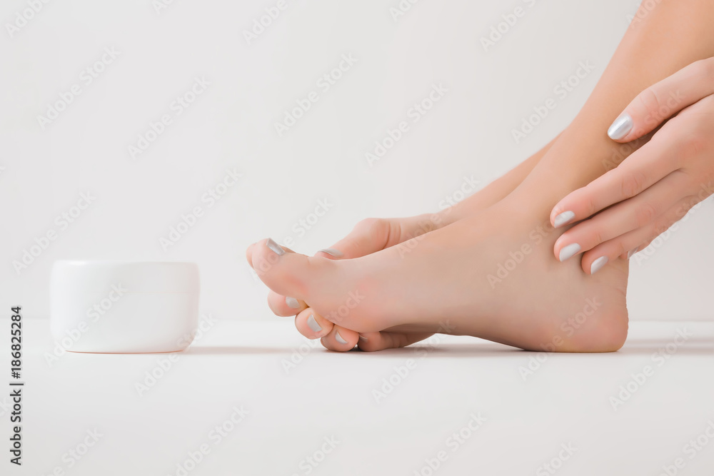 Fototapeta premium Barefoot with cream jar. Cares about a woman's clean and soft foot skin. Body care concept.