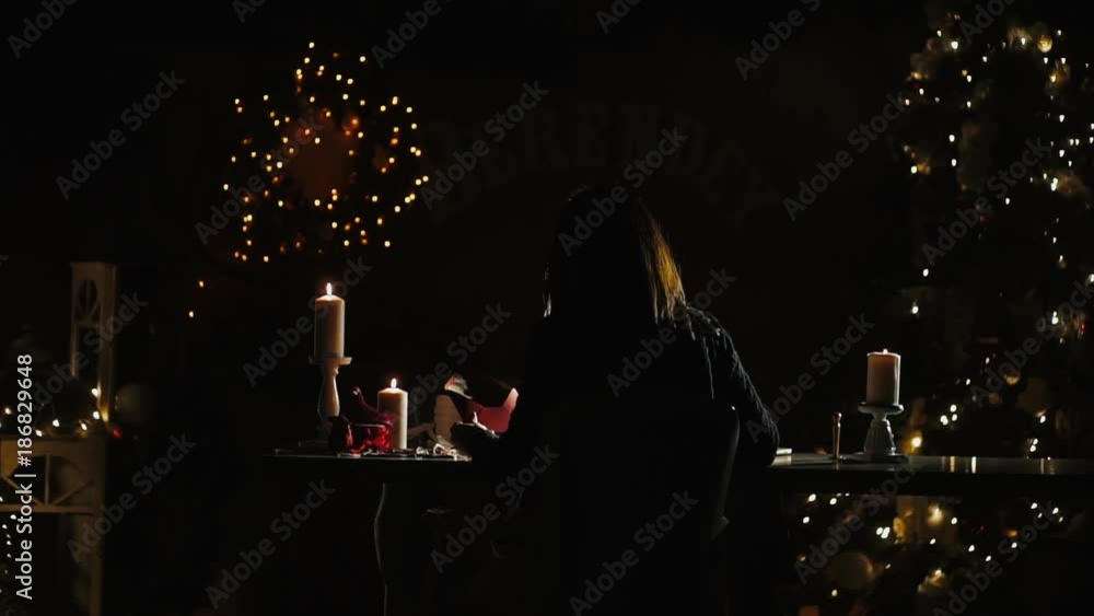 Girl writes a pen, a caligraphic handwriting, in a New Year's atmosphere a letter to her beloved. Sitting at a table with candles, next to decorated New Year trees, waiting for Christmas. 2020