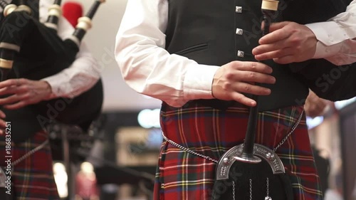A man in a Scottish kilt is playing on a bagpipe. Concert. Bagpipes. A man in checkered clothes. Musician at the concert.