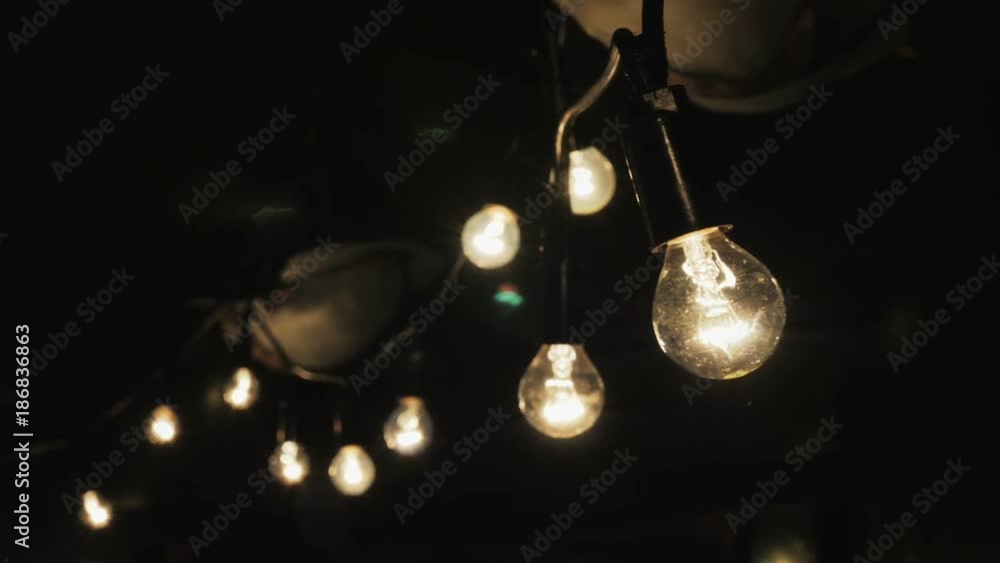 Decorative string lights hang and glow outdoors at night. Warm lighting, garland of lamps or glass lantern. Decorative string lights hang and glow outdoors at night. Warm lighting, garland of lamps or glass lantern.