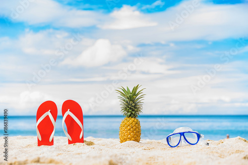 Close up Pineapple, mask and filp flop on the beach with blue sky and sea on background. photo