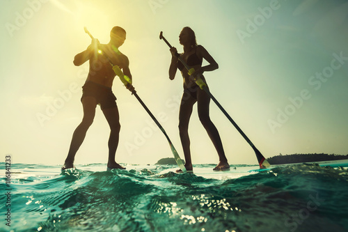 Paddleboarding at sunset. Young couple in the sea with paddle and board. photo