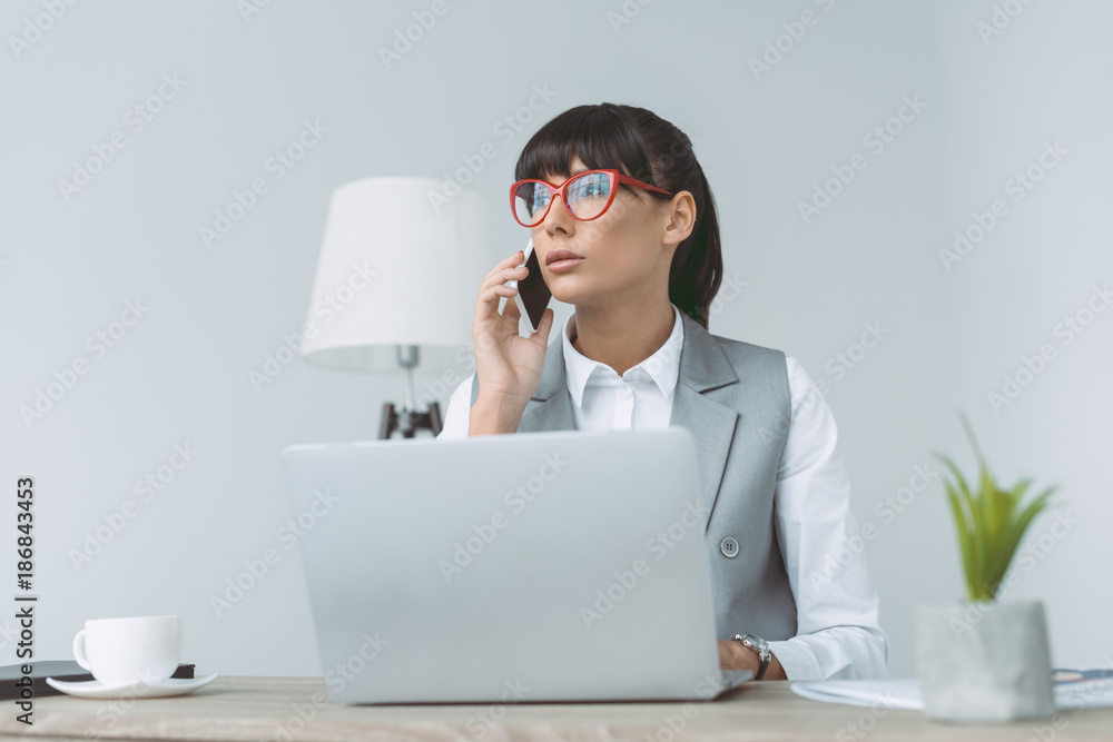 businesswoman talking by smartphone and using laptop isolated on gray businesswoman talking by smartphone and using laptop isolated on gray