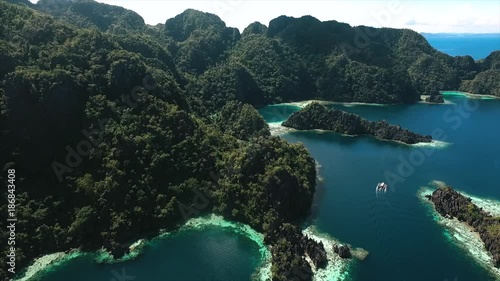 Aerial view flying over amazing white sand beach and tropical coral reef lagoon towards beautiful green mountains on Simizu island photo