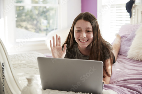 Teen girl lying on bed making a video call with laptop