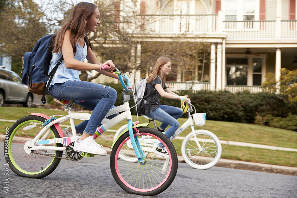 Two teen girls riding bikes in street, side view close up