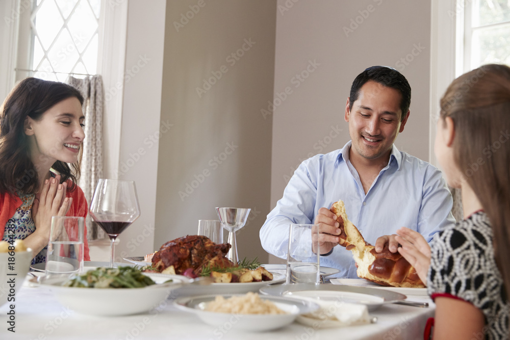 Jewish man sharing challah bread with family at Shabbat meal Jewish man sharing challah bread with family at Shabbat meal