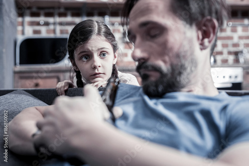 Careless father. Sad cheerless cute girl looking at her father and being upset while seeing his drinking