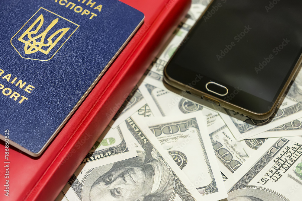 Ukrainian passport on the background of hundred-dollar bills along with a phone and a card. Ukrainian passport on the background of hundred-dollar bills along with a phone and a card.