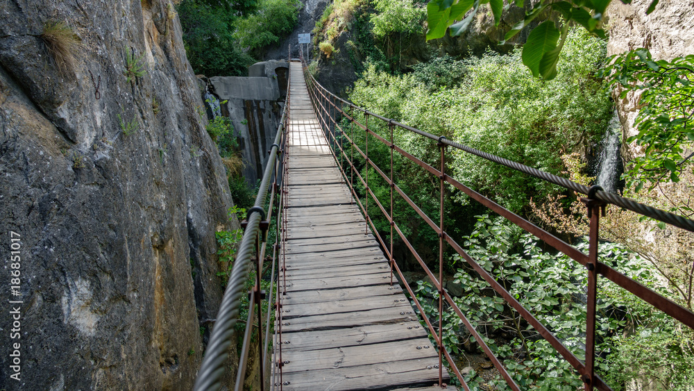 Iron and wooden suspension bridge in canyon between vertical rocks Iron and wooden suspension bridge in canyon between vertical rocks