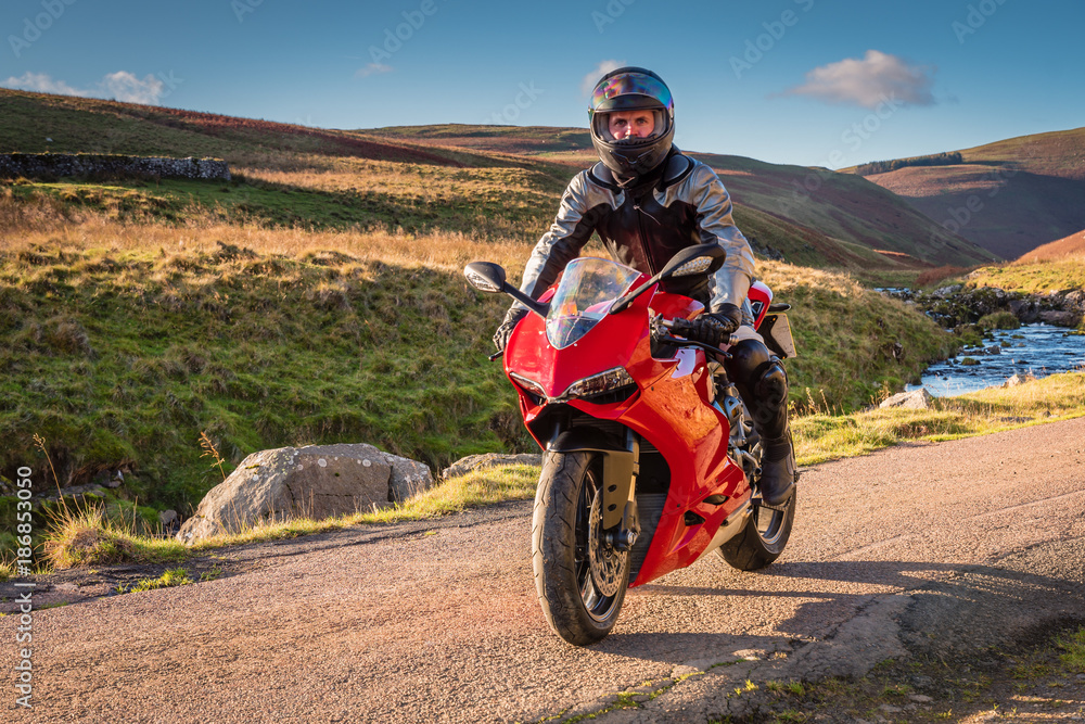 Motorbike on country road / Red Motorbike with rider in Upper Coquetdale, Northumberland on a sunny day Motorbike on country road / Red Motorbike with rider in Upper Coquetdale, Northumberland on a sunny day
