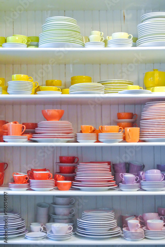 Bright colorful yellow red dishes, plates and cups standing on white shelf. Concept of buying choosing new dishes for house home, interior indoor decoration o for gifts. Clean ordered dishes in store.