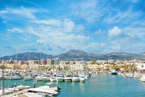 Benalmadena Puerto Marina sport port, a view to piers with white modern luxury sport yachts, Mediterranean sea and mountains and cloudy sky at the background. Spain winter relax vacation concept. photo